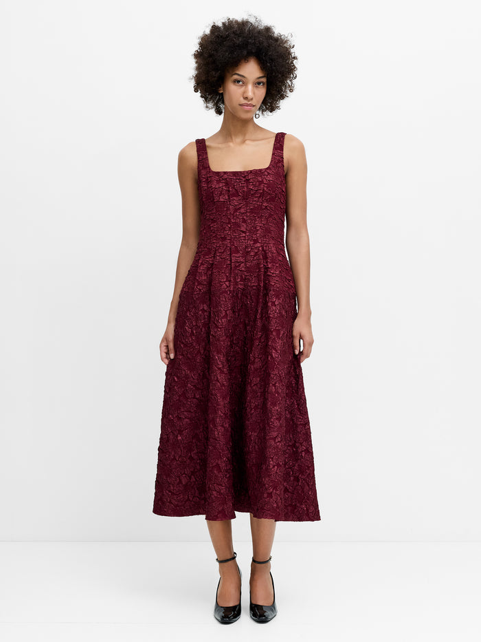 A woman wearing a burgundy floral jacquard midi dress with a square neckline, invisible back zip and fit and flare silhouette.