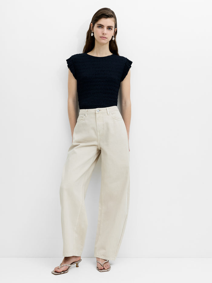 A woman wearing high waisted, relaxed cream curved leg jeans with a fly zip and belt loops.