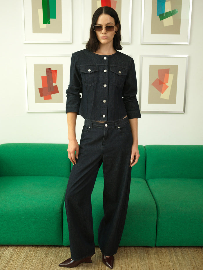 A woman wearing high waisted, dark blue jeans with a fly zip, belt loops and a curved fit.