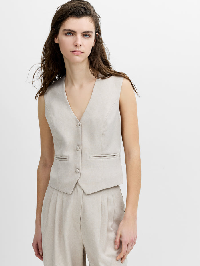 Woman wearing a tailored beige fitted sleeveless v-neck waistcoat, featuring a button down fastening and two pockets.
