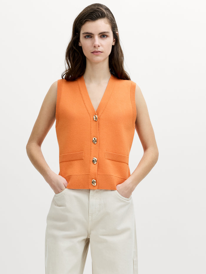A woman wearing an orange knit waistcoat with a V-neck neckline, button down fastening and a fitted silhouette.