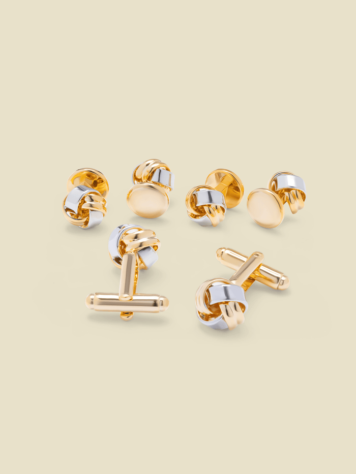 Gold and silver knot-shaped cufflink and stud set, six pieces, on a cream background.