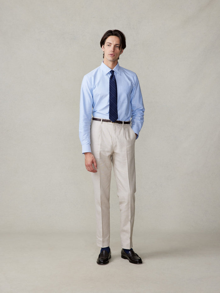 Man in mojave tan linen pants, light blue shirt, navy striped tie, full length, hand in pocket