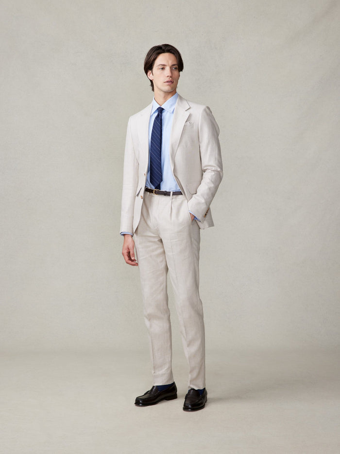 Man in mojave tan linen suit, navy striped tie, three-quarter turn, hand in pocket, full length