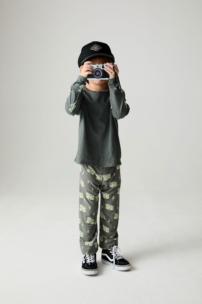 A full body front view of a boy wearing the Chaser Monster Truck Pants Boys Jogger on a neutral background holding a camera