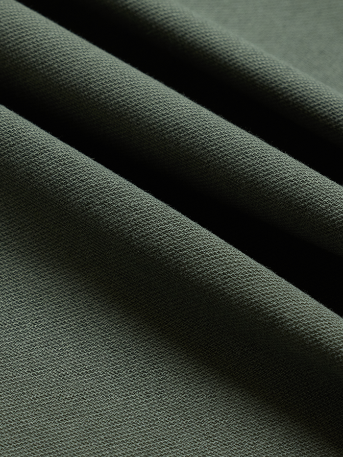 Close-up of moss green cotton pique fabric with folds, showing textured weave