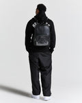 Person wearing a black tracksuit with a backpack on a white background