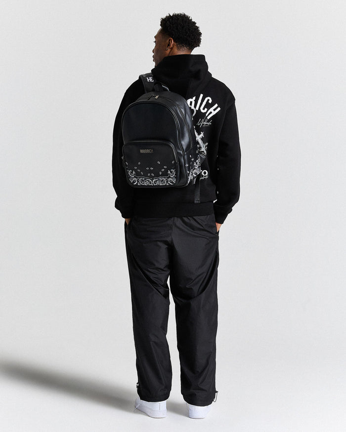 Person wearing a black hoodie with a brand logo and a black backpack on a white background