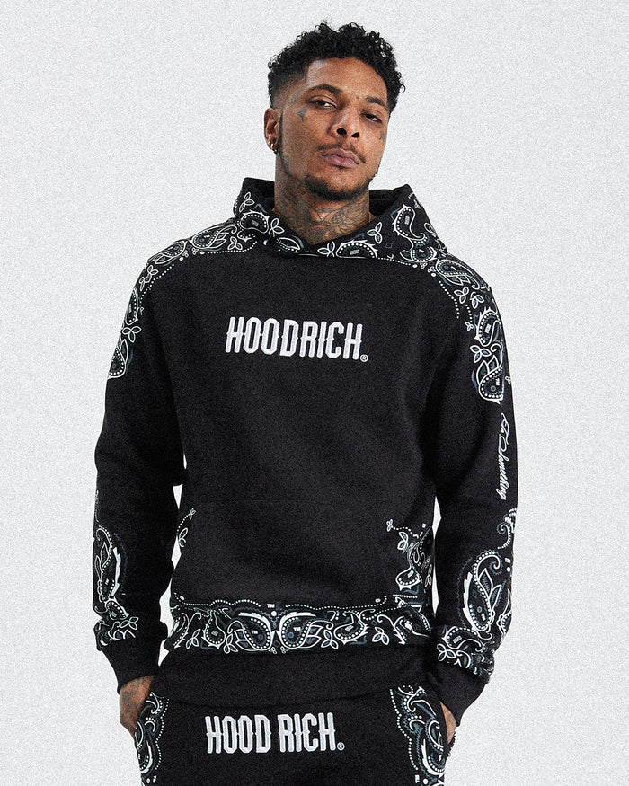 A male model wearing a black hoodie with 'HOODRICH' text and motif print design.