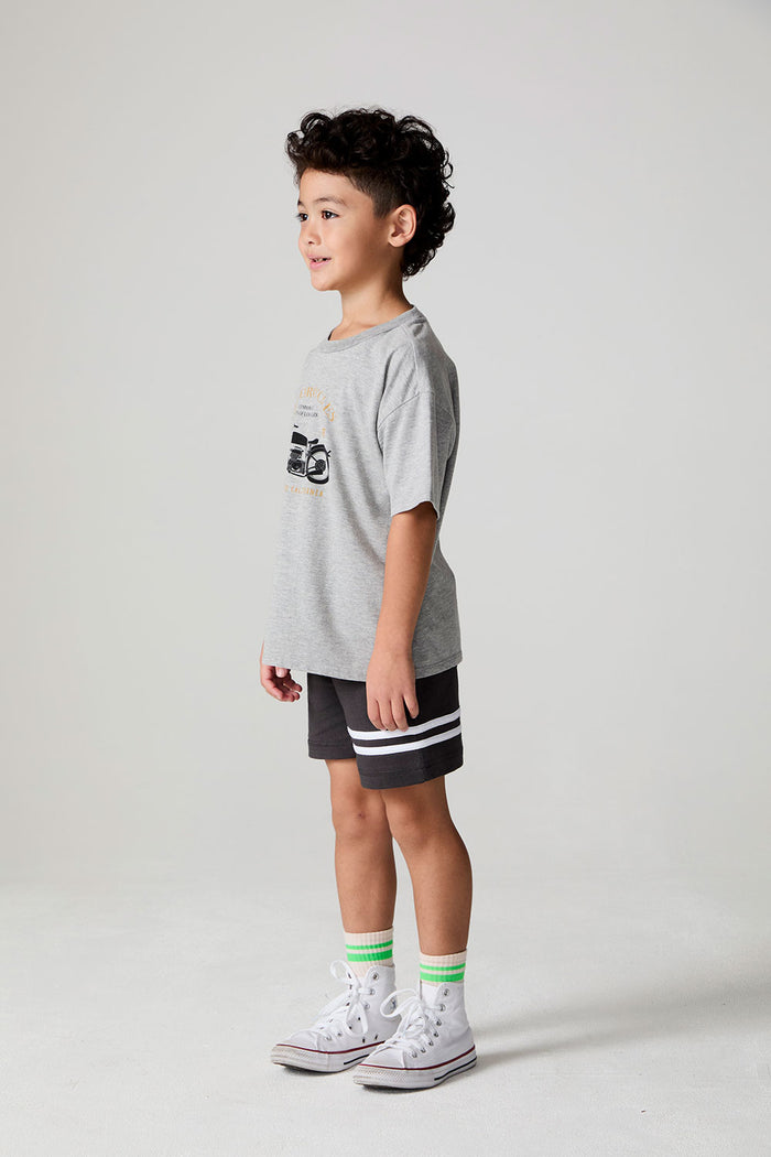 Full body side angle view of a boy wearing the Chaser  Moto LA Tee on a neutral background