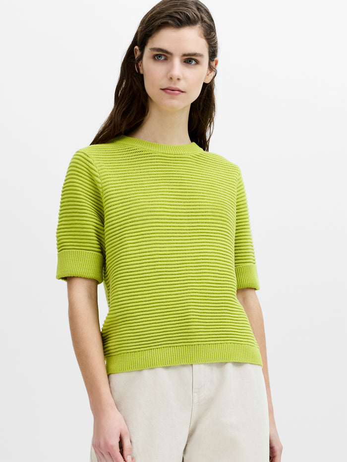 Woman wearing a boxy fit, crew neck ribbed knit jumper with short sleeves and turn up cuffs.