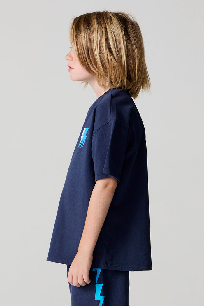 Side view of a boy wearing the Chaser Multi Bolt Tee on a neutral background