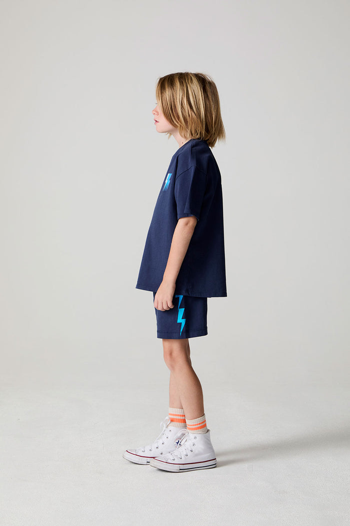 Full body side view of a boy wearing the Chaser Multi Bolt Tee on a neutral background