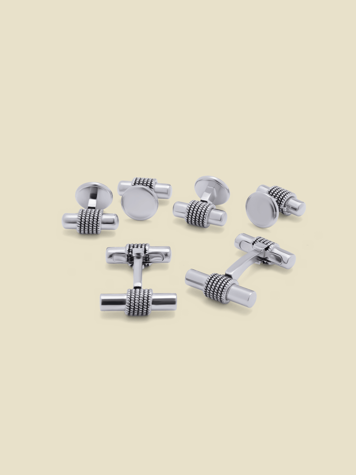 Silver-tone cufflink and stud set with rope-wrap tube centers, on a cream background.