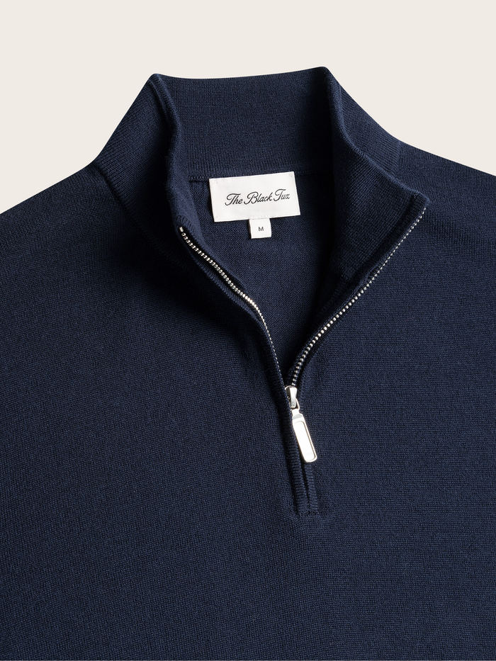 Close-up of navy quarter-zip sweater collar and zipper pull with brand label