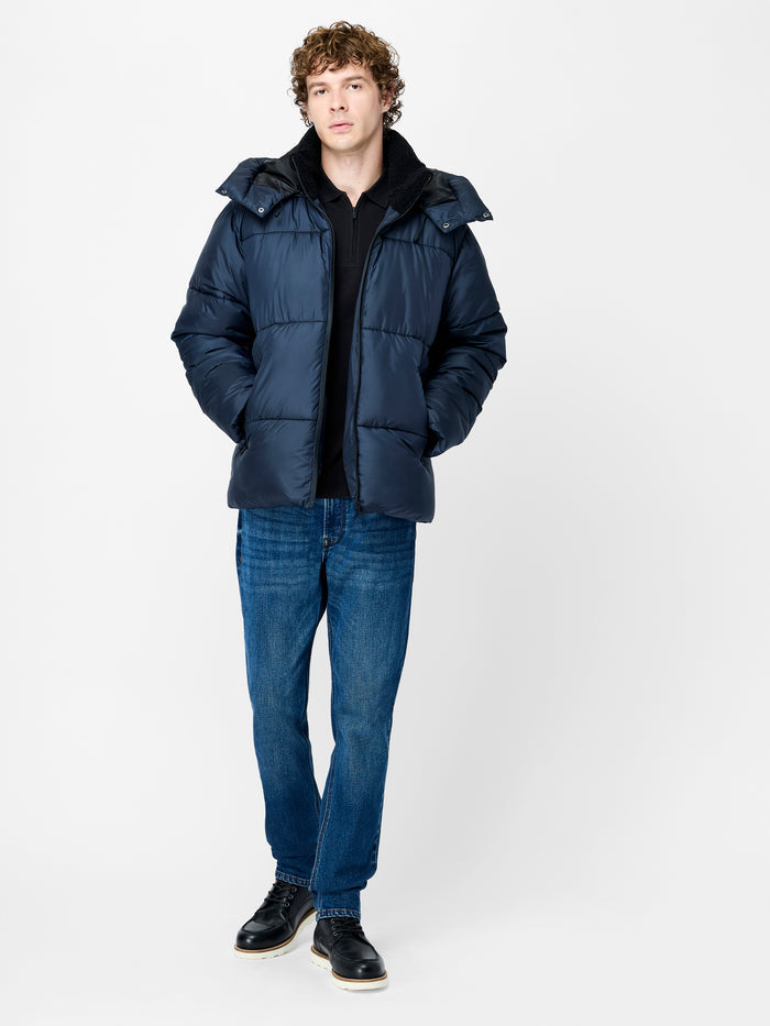 A man wearing a navy blue smooth padded puffer Jacket with a removable hood, long sleeves with inner cuffs and a zip through fastening.