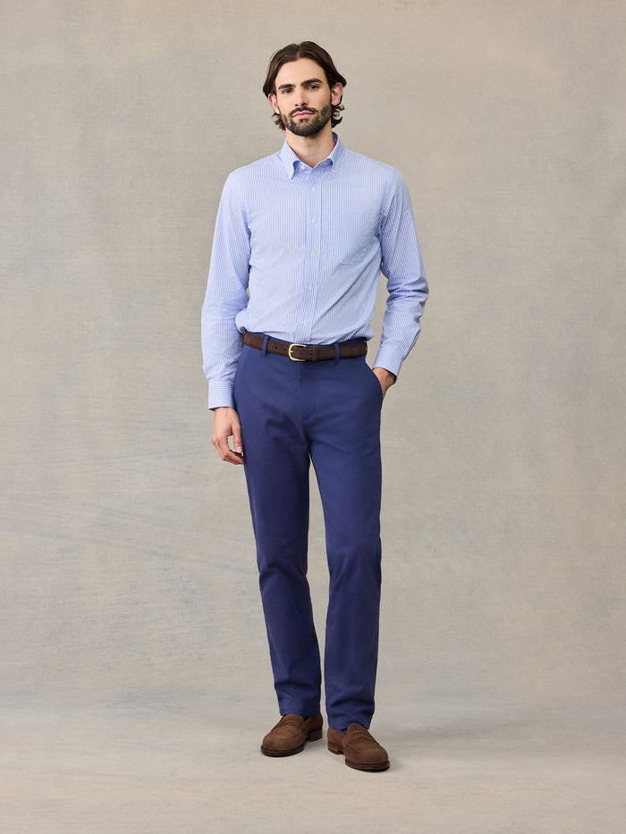 Man in navy chino pants and light blue striped shirt, hand in pocket, full length