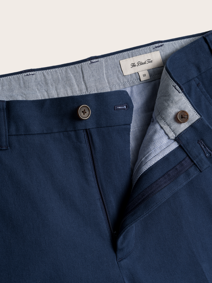 Close-up of navy chino pants waistband, button fly, and brand label