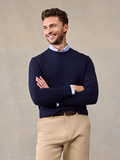 Smiling man in navy crewneck sweater over light blue collared shirt, arms crossed, khaki pants