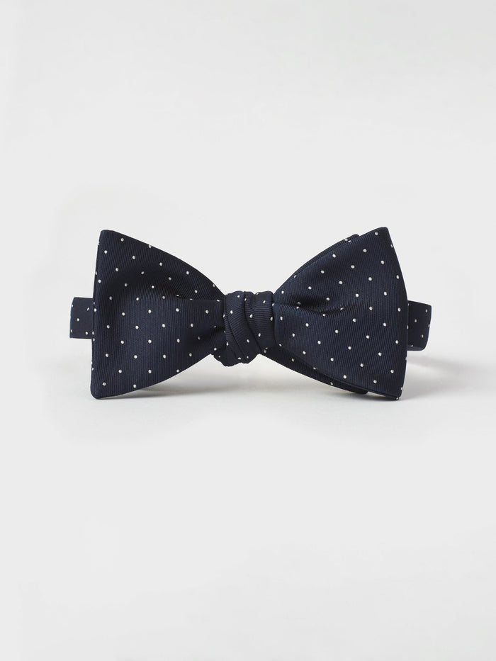 Navy bow tie with white polka dots, tied, on a light grey background