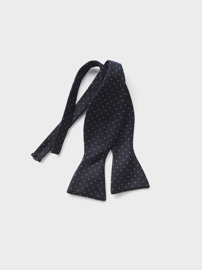 Navy bow tie with white polka dots on a light background.