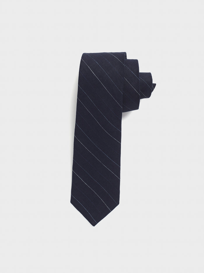 Navy pinstripe linen necktie rolled into a coil on light grey background