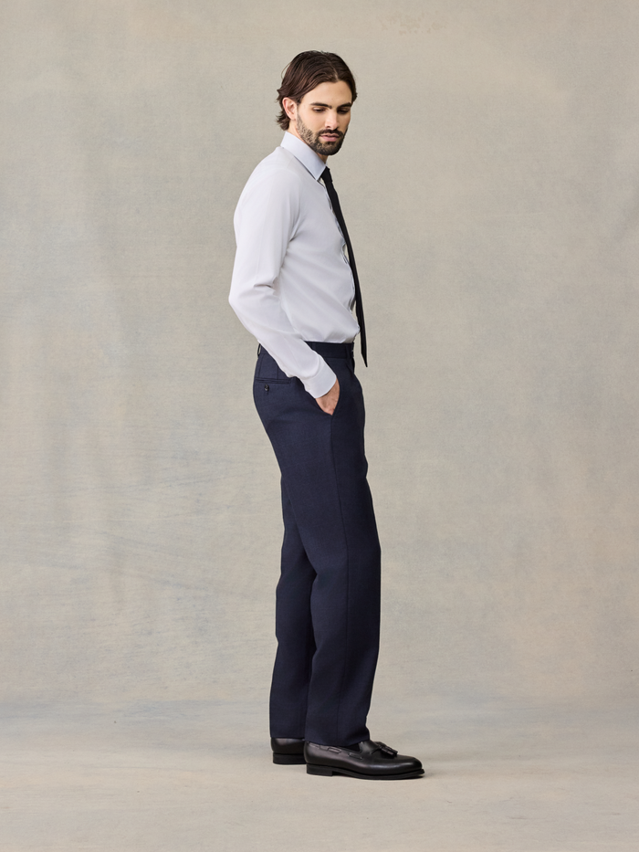 Side profile of man in navy plaid wool suit pants and white shirt with black tie, hand in pocket