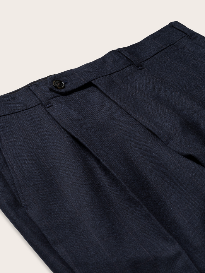 Close-up of navy plaid wool suit pants waistband, pleat, and button tab
