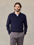 Smiling man in navy long-sleeve polo sweater over white tee, grey pants, hands in pockets