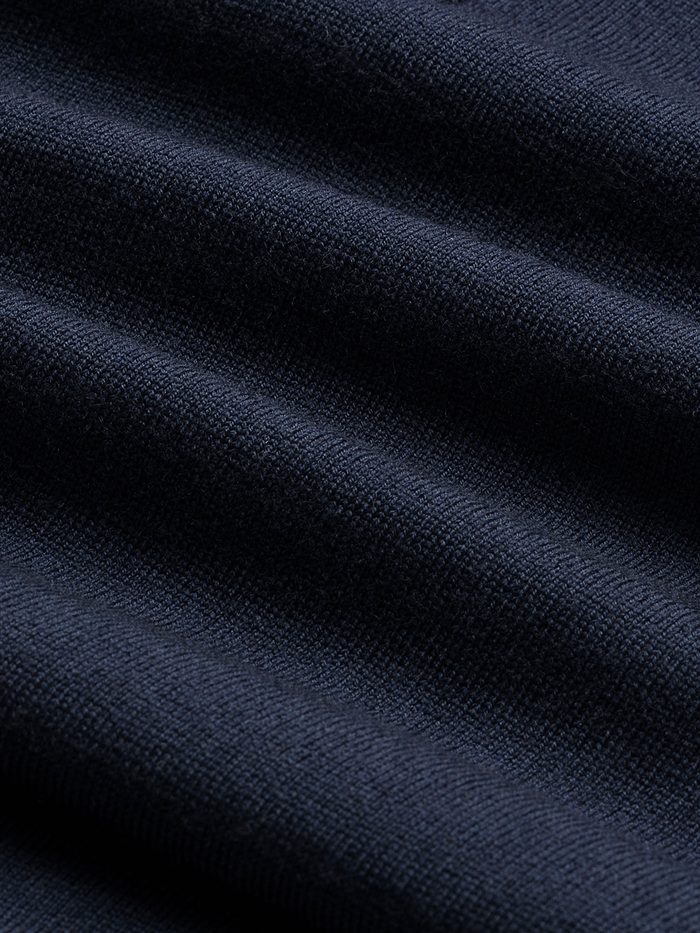 Close-up of navy sweater knit fabric with folds, showing fine-gauge texture