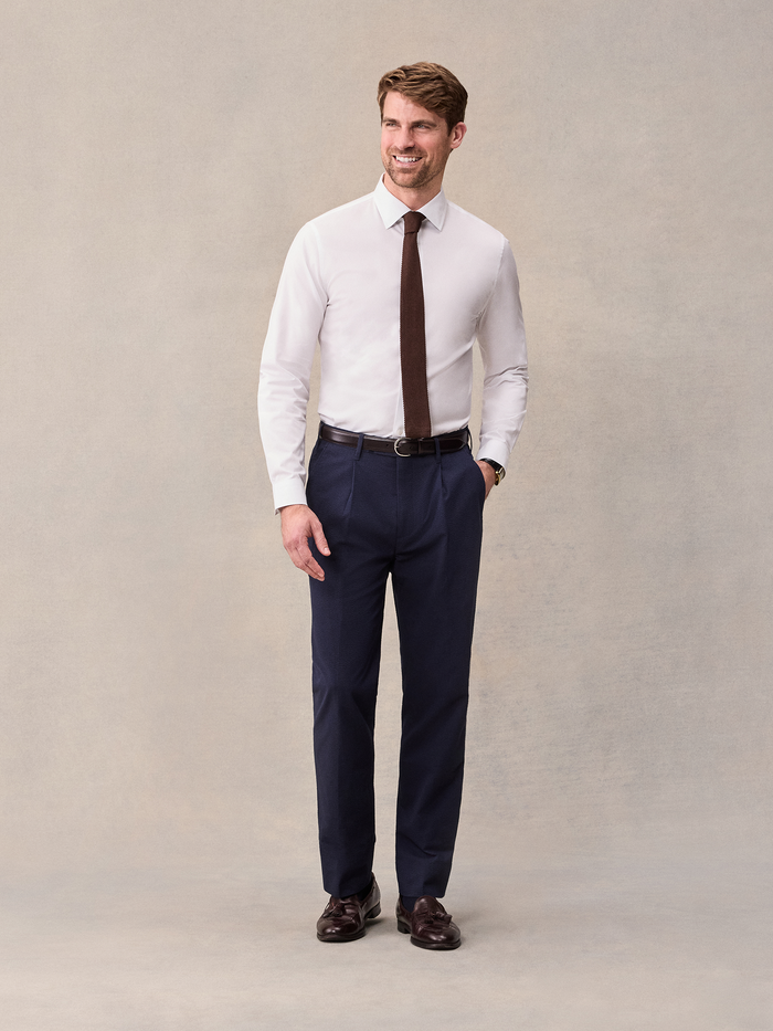 Smiling man in white shirt with brown knit tie and navy seersucker pants, full length
