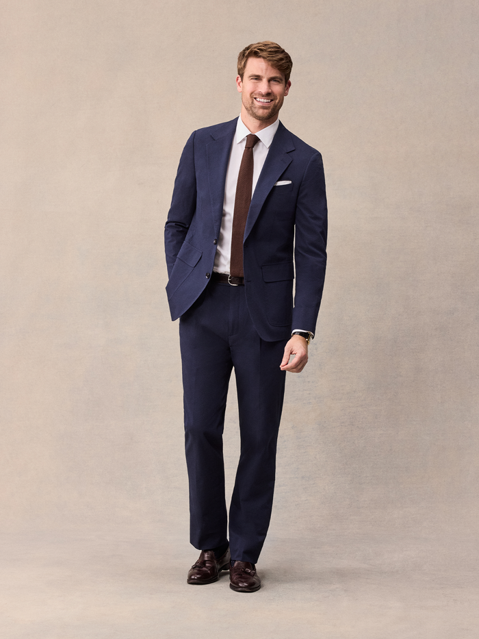 Smiling man in navy seersucker suit with brown knit tie, full length, front view
