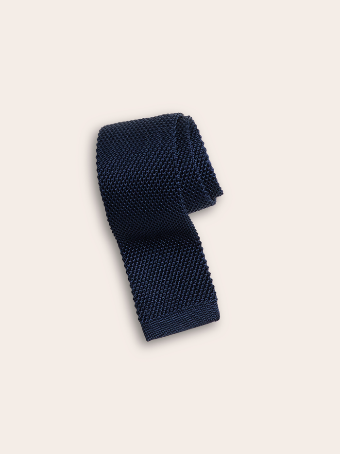 Navy silk knit tie rolled into a coil on light grey background