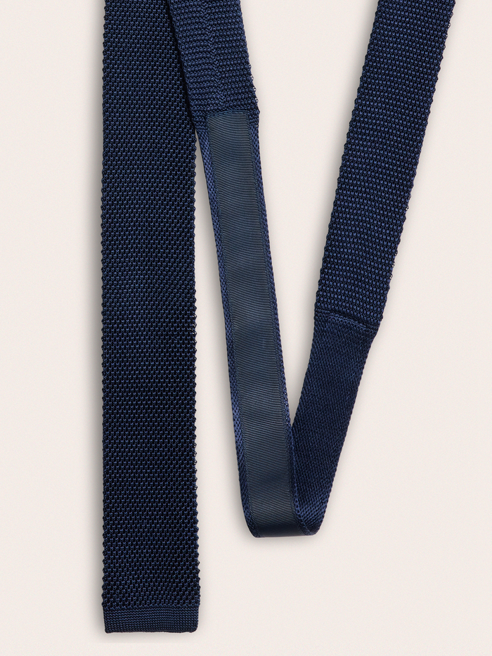 Navy silk knit tie draped in a loop, showing back seam and knit texture