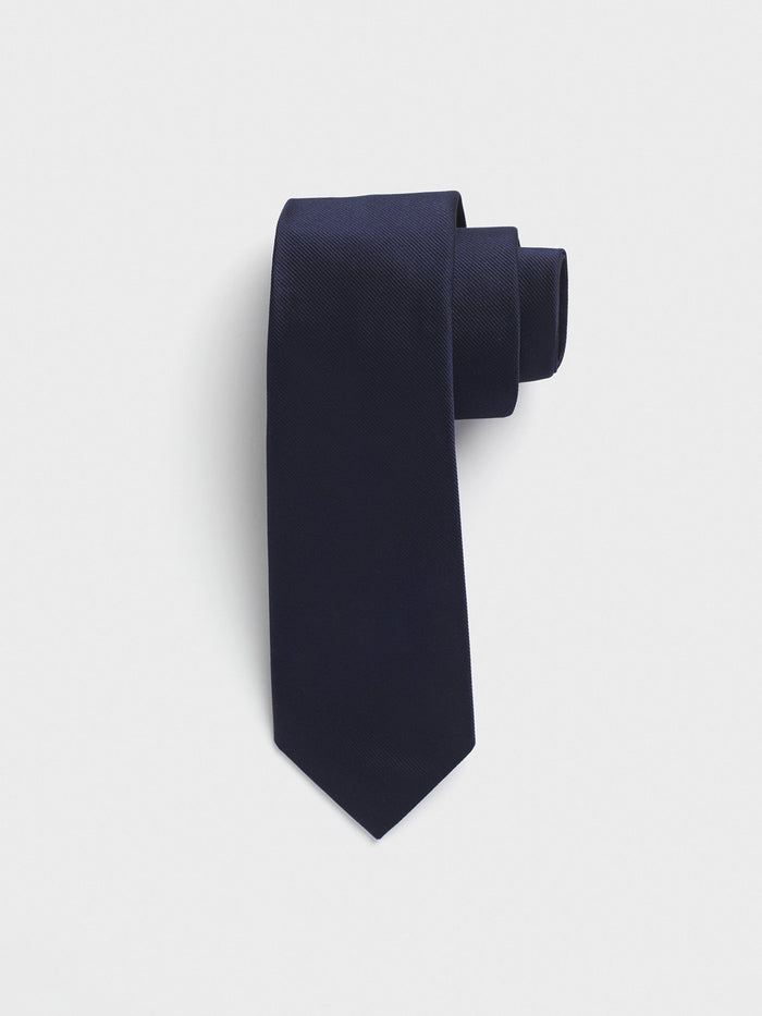 Navy silk necktie rolled into a coil on light grey background