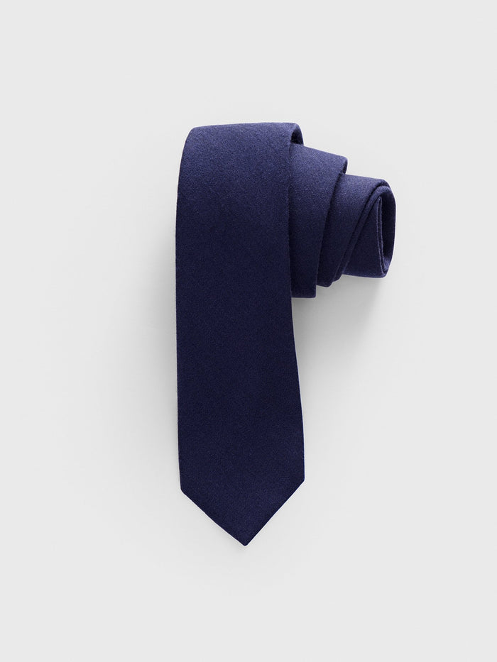 Navy wool-silk necktie rolled into a coil on a light grey background