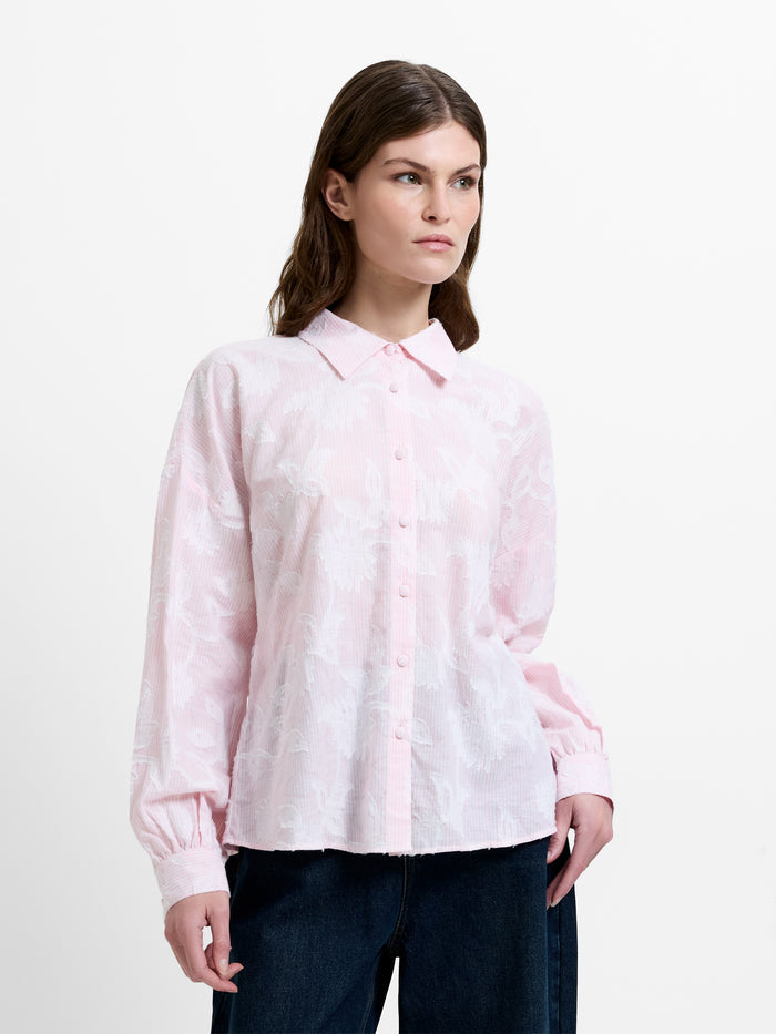 Woman wearing a light pink and white floral jacquard shirt, with dropped long balloon sleeves and a shirt collar