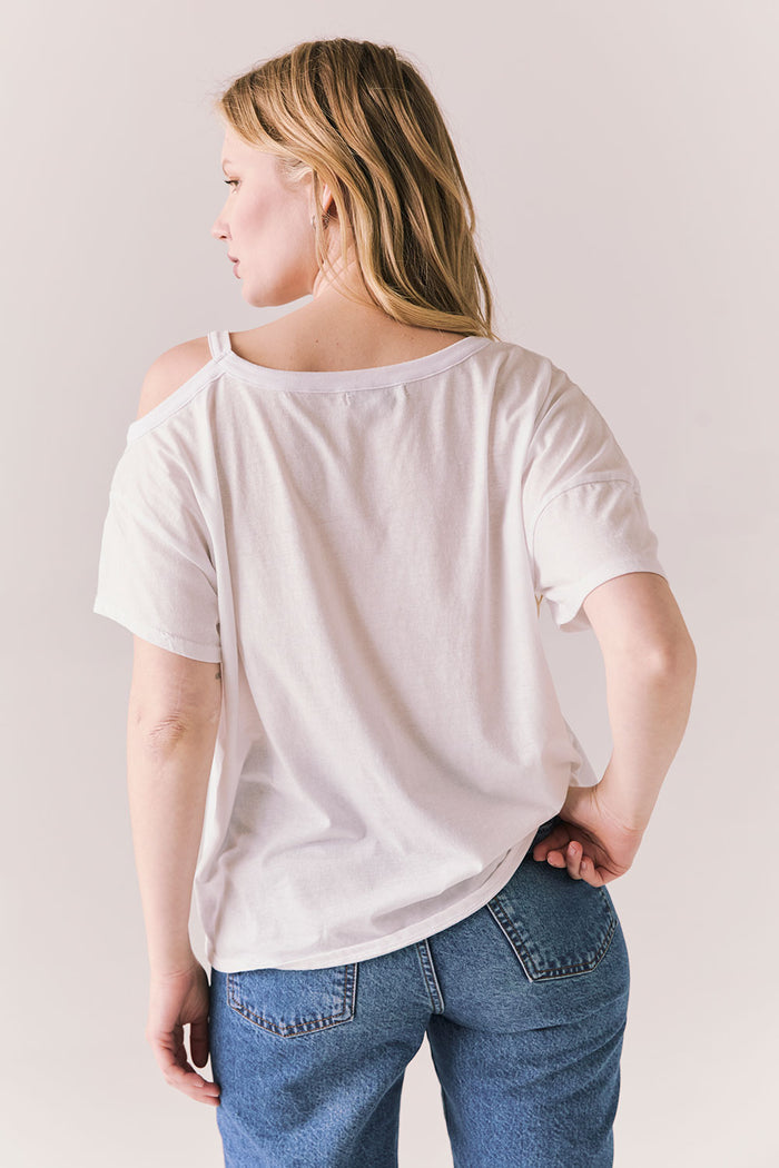 Back view of Northridge Tee in white with cold shoulder cutout and flowy fit and blue jeans against a plain background