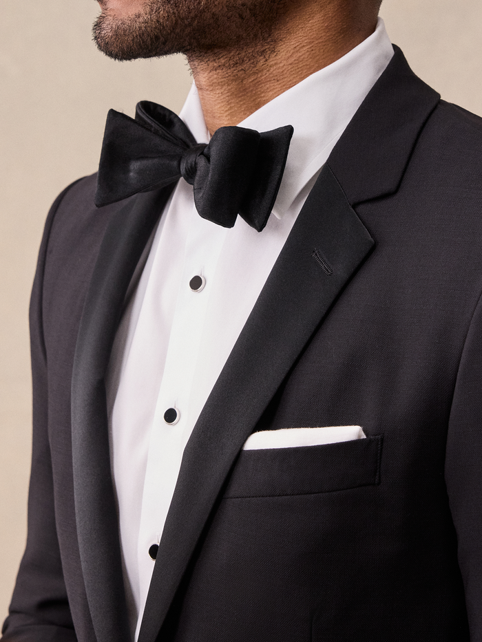 Close-up of black bow tie and notch lapel on tuxedo jacket, white shirt with black studs