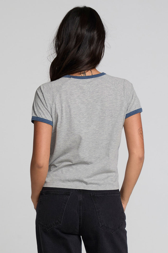 Back view of a woman wearing the Chaser NYC 68 Ringer Graphic Tee and black jeans on a neutral background with arms lowered