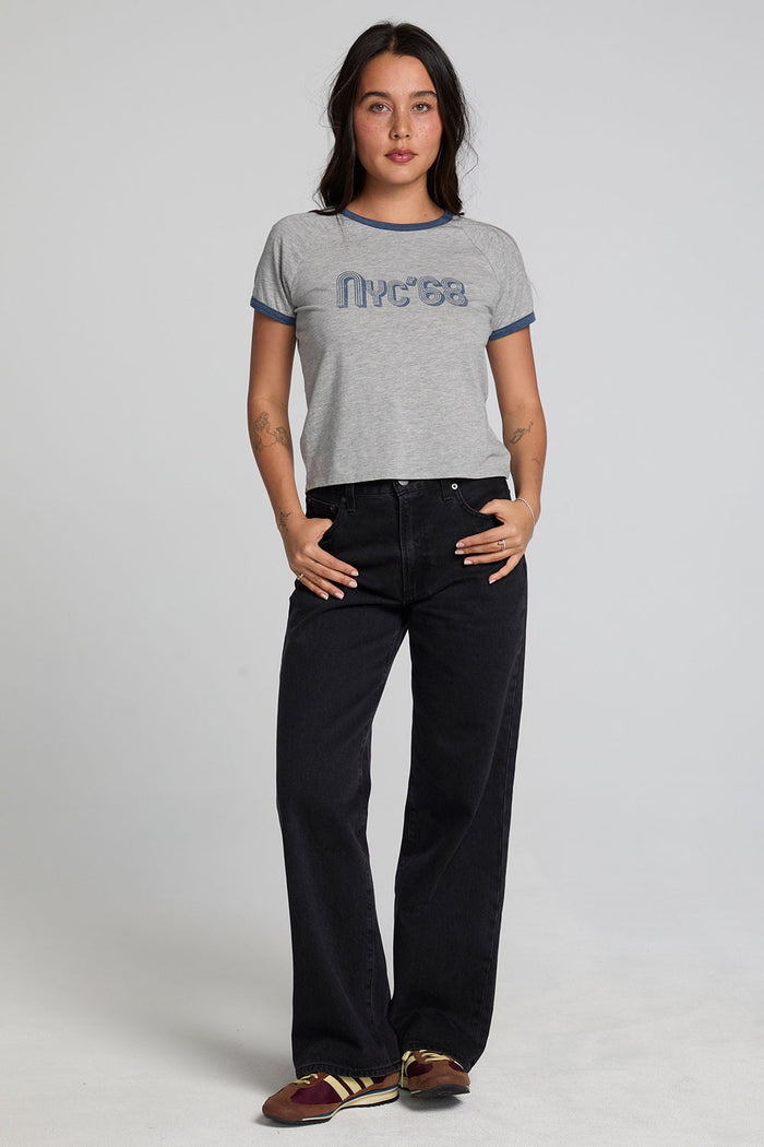 Full body front view of a woman wearing the Chaser NYC 68 Ringer Graphic Tee and black jeans on a neutral background with arms on hips