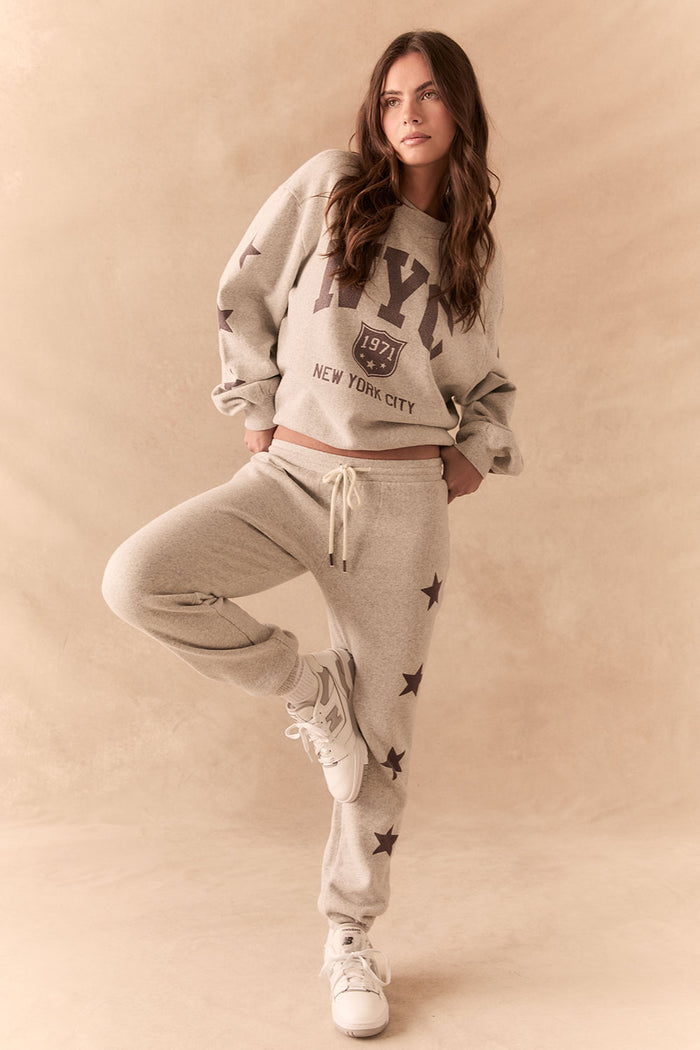 Full front view of NYC Stars Joggers in Heather Grey with smoky plum star print down each leg and matching top, styled for a casual lounge look, against a beige background