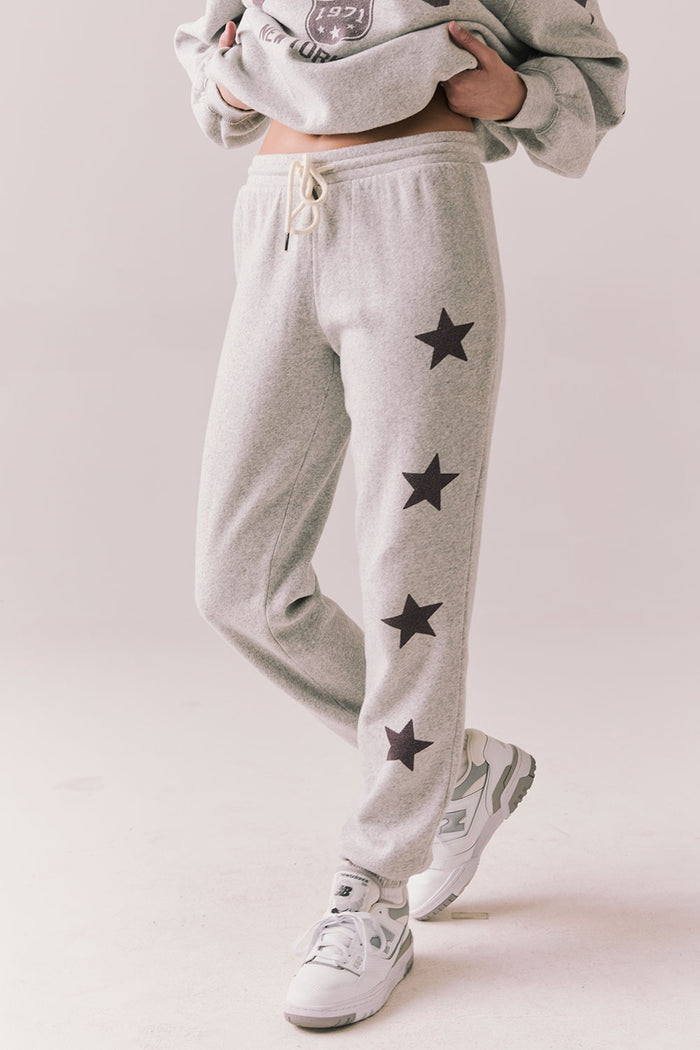 Side view of NYC Stars Joggers in Heather Grey with smoky plum star print down each leg, styled for a casual lounge look, against a plain background