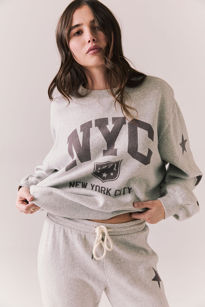Front view of NYC Stars Pullover in Heather Grey with bold chest lettering and smoky plumb star sleeves against a plain background