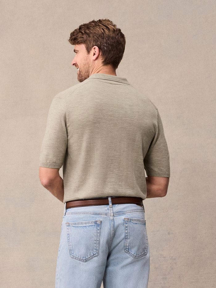 Back view of man in oatmeal knit polo and light wash jeans against beige backdrop