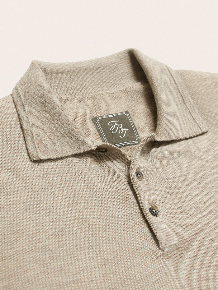 Close-up of oatmeal knit polo collar and buttons with brand tag, on cream background