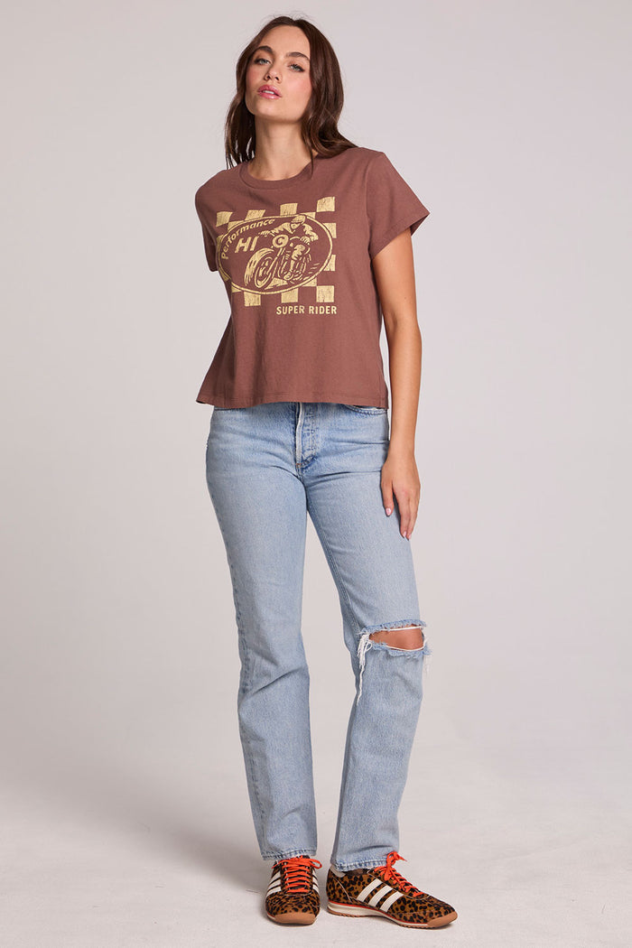 Full body front view of a woman wearing the Chaser Off Road Race Team Graphic Tee and blue jeans on a neutral background with arm at side