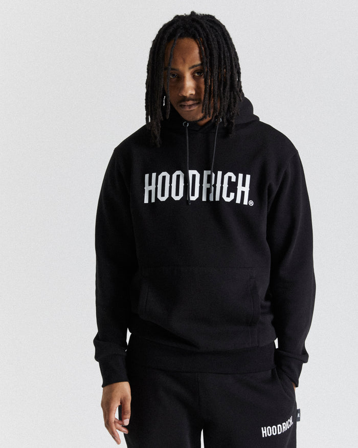 A male model wearing a black hoodie with 'HOODRICH' text on the front, paired with black pants, standing against a white background.