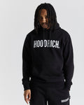 A male model wearing a black hoodie with 'HOODRICH' text on the front, paired with black pants, standing against a white background.