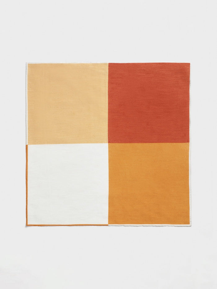 Pocket square in four color blocks: pale yellow, rust orange, cream, and marigold, laid flat, white background.